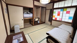Una habitación tradicional japonesa con suelo de tatami, futón, un pequeño escritorio con silla y ventana con bloques de papel de colores.