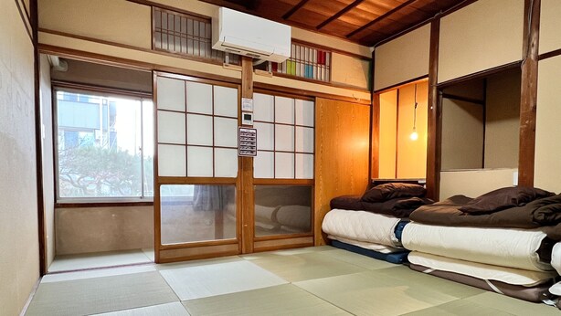 Una habitación japonesa tradicional con suelo de tatami, un futón, puertas correderas shoji y una ventana pequeña.