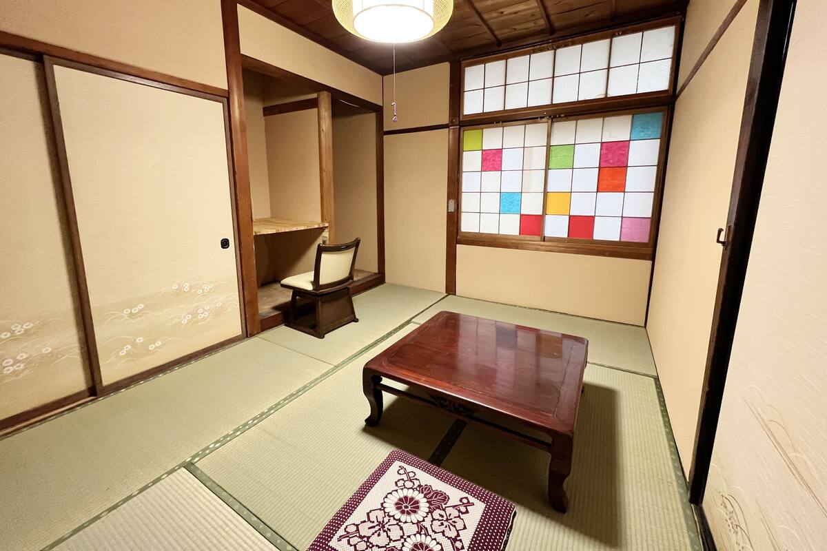 Ett traditionellt japanskt rum med tatamimattor på golvet, ett träbord, en stol och en shojiskärm med färgglatt papper.