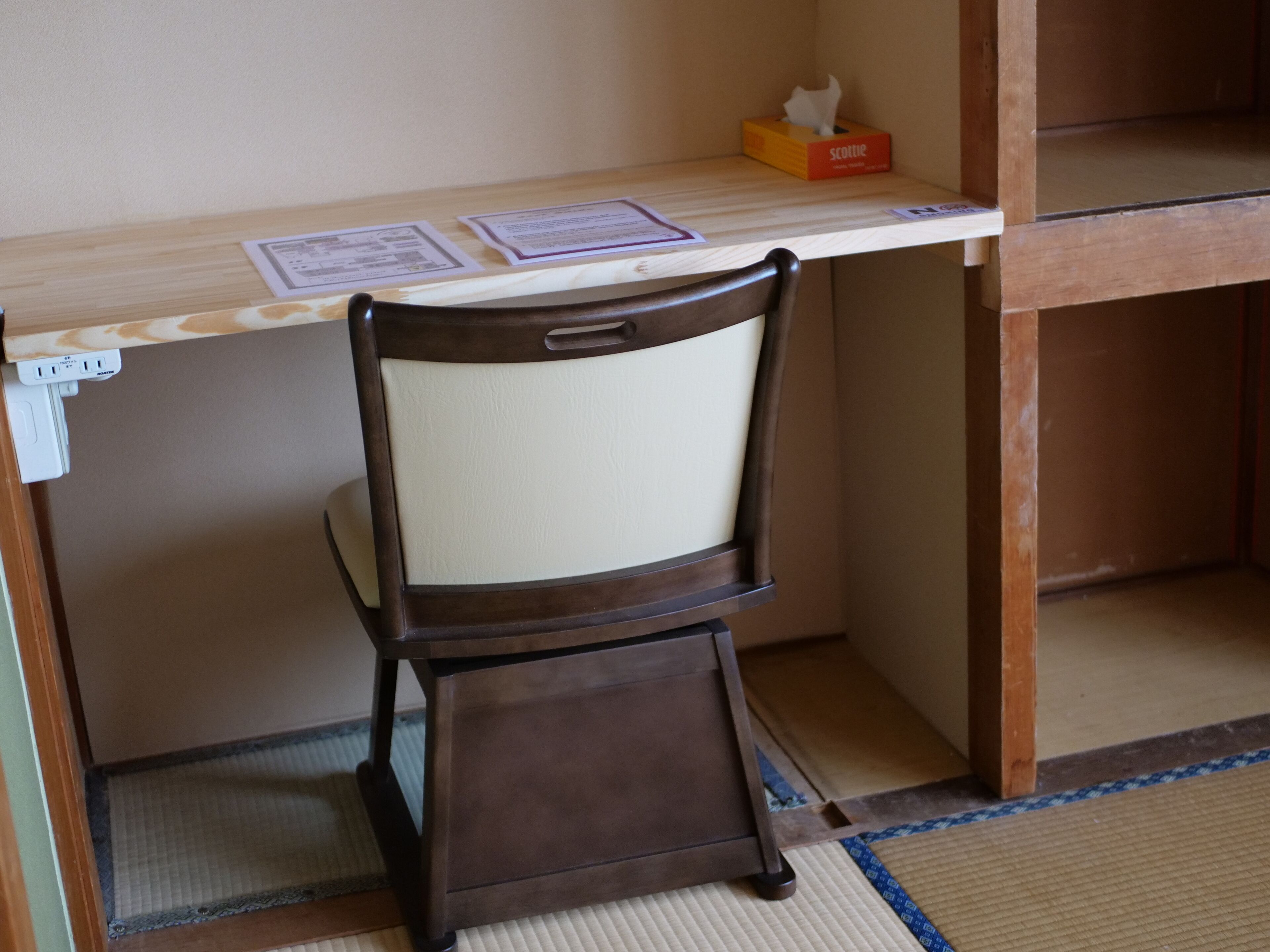 A wooden desk with a chair, a tissue box, and some papers on it.
