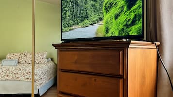 A bedroom with a bed, a wooden dresser, a television on top of the dresser, and a ceiling fan.