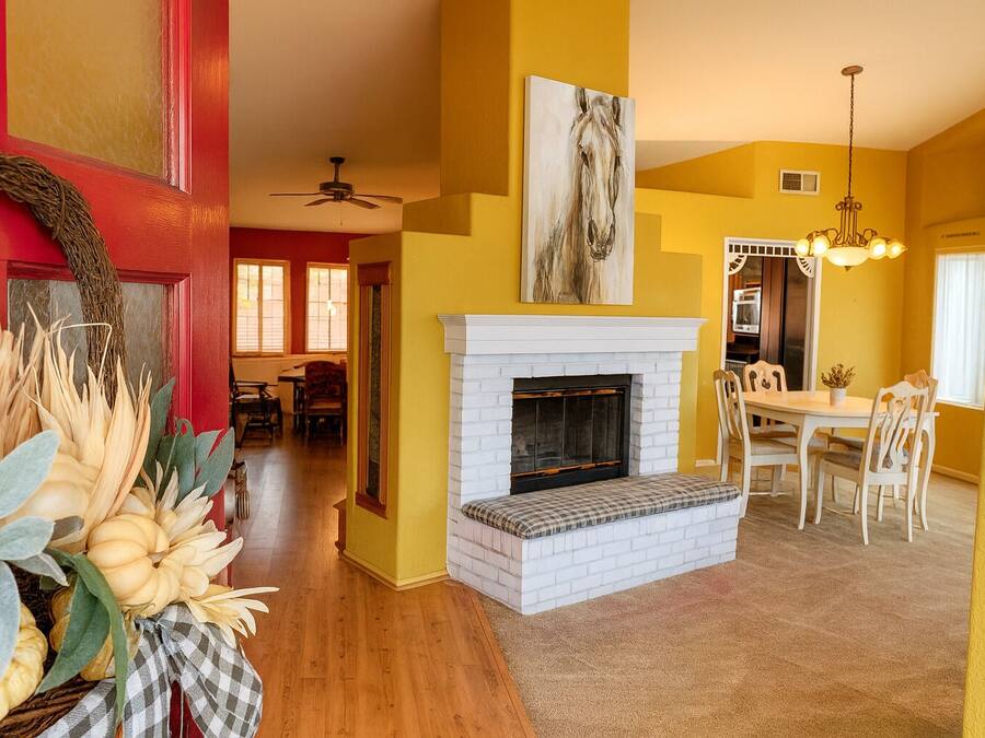 Una sala de estar con chimenea, paredes amarillas y una zona de comedor con candelabro.