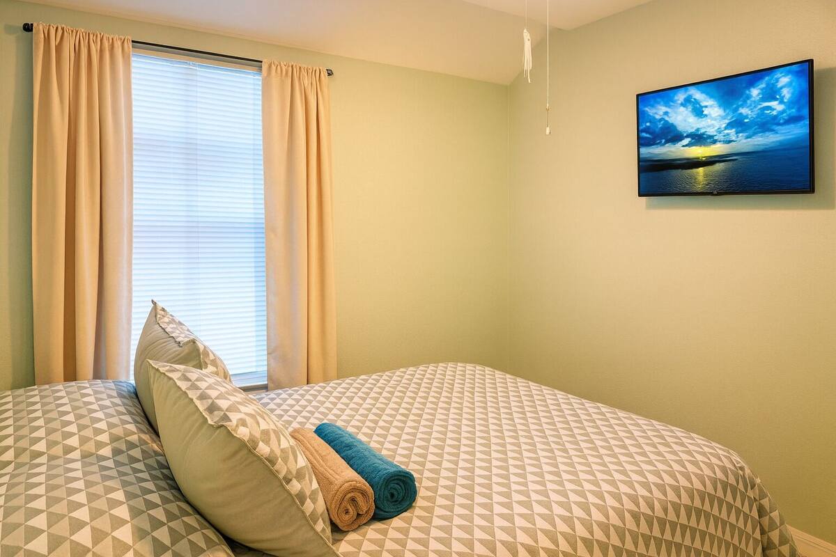 A bedroom with a bed, a window with curtains, and a painting on the wall.