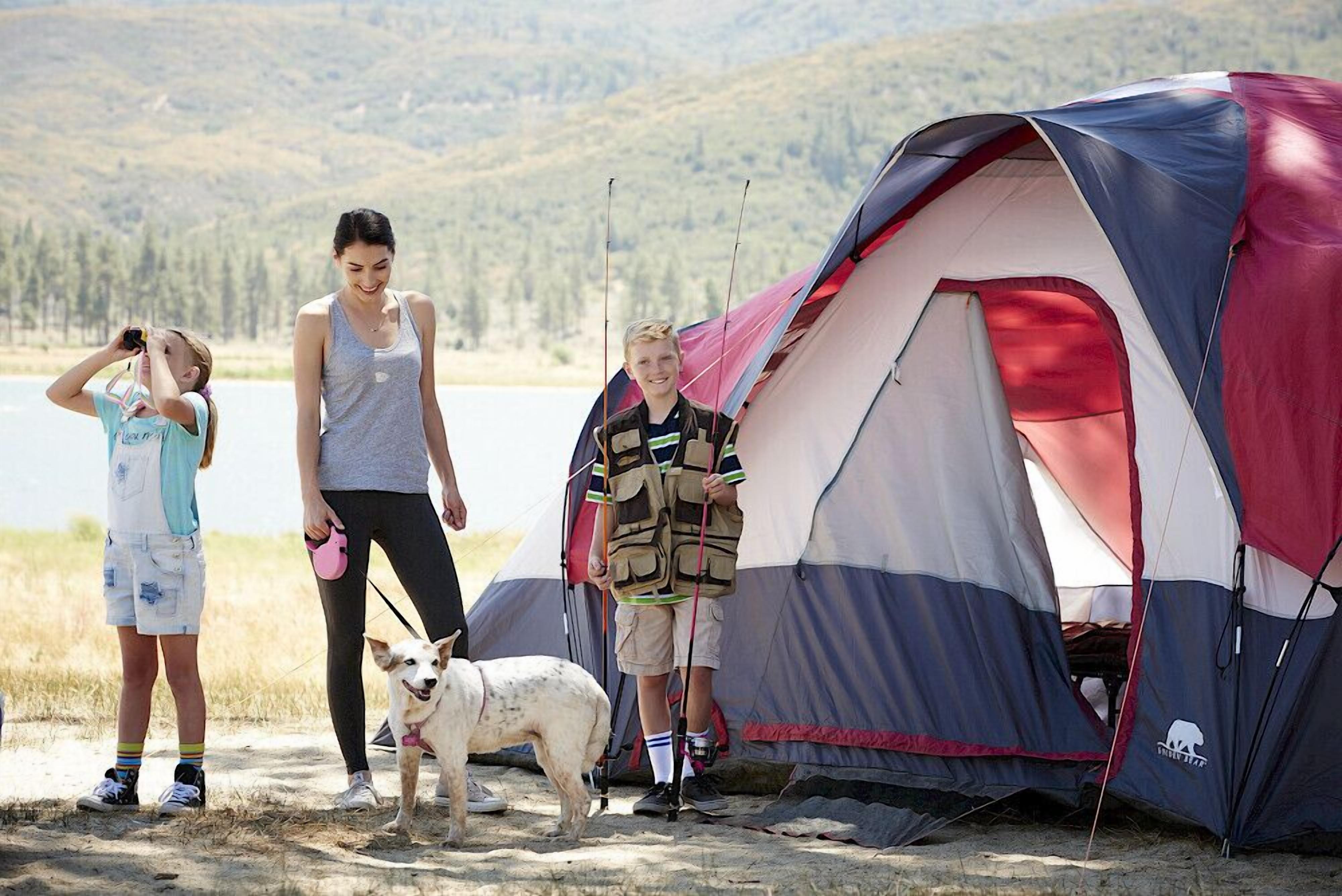 A group of people near a tent with a lake and hills in the background.