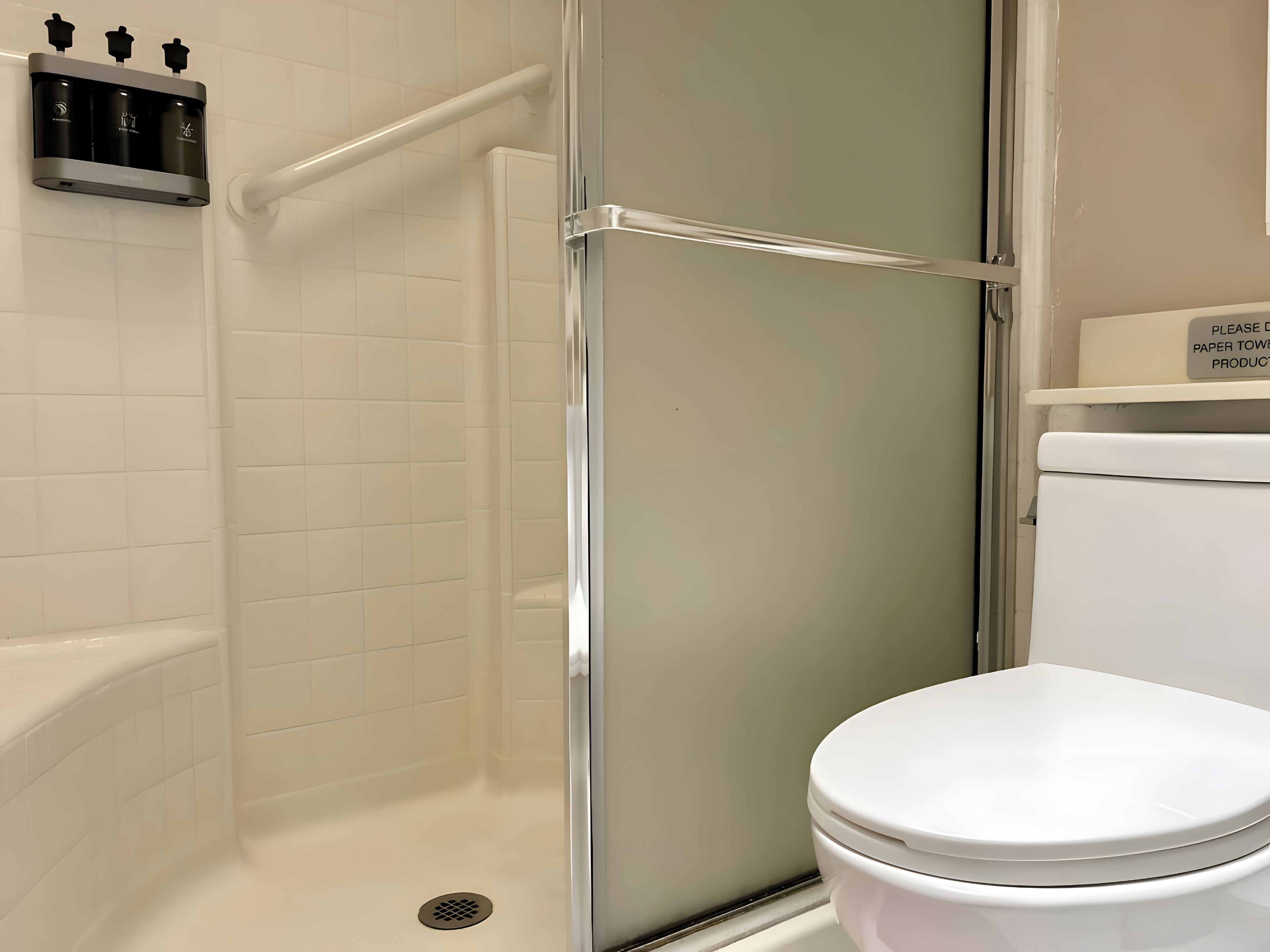 A modern bathroom with a glass-enclosed shower, a white toilet, and a soap dispenser mounted on the wall.