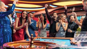 Een groep mensen viert in een casino, met een roulette tafel op de voorgrond.