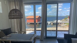 A room with a dining table and chairs, a wicker lamp, a sofa, and a view of a dock with boats and a red building by the water. - Fantastic location next to Lake Sommen (Ydre)