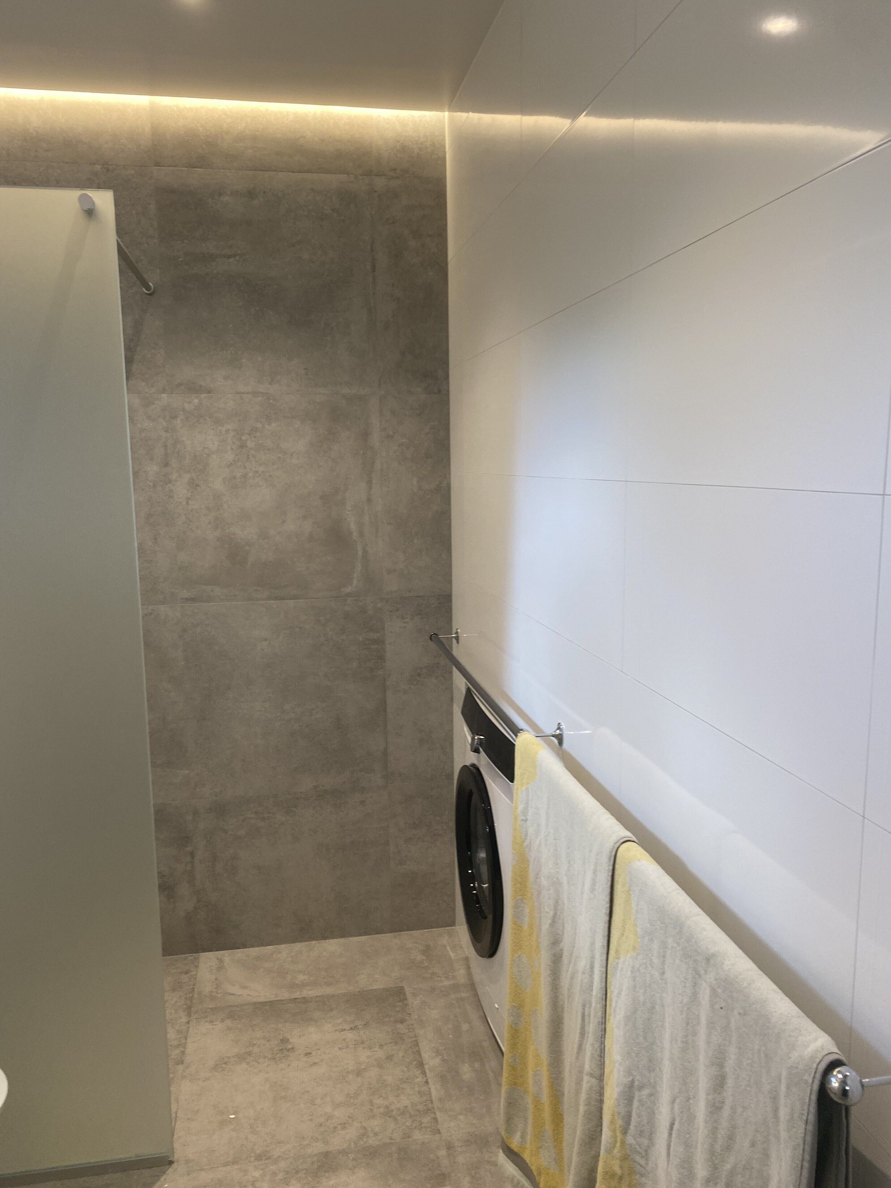 A modern bathroom with a built-in washing machine, a towel rack, and a shower area.