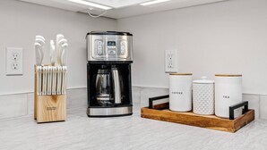 Een moderne keuken met een koffiezetapparaat, een messenblok en twee containers met daarop 'koffie' en 'thee'.