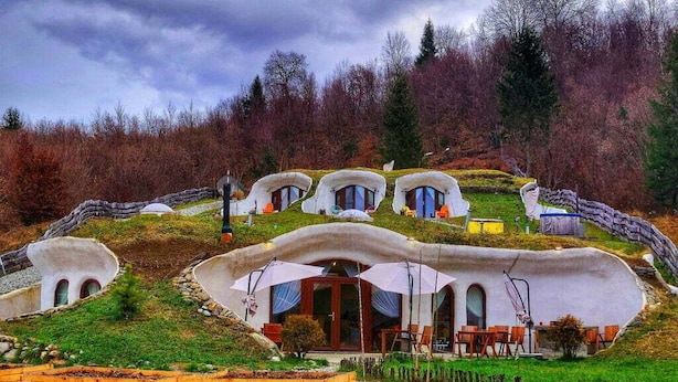 A series of geodesic dome structures with multiple rooms, each featuring a door and windows, surrounded by a landscaped garden and a forested hillside. - Pensiunea Dealul Verde (Sibiu)