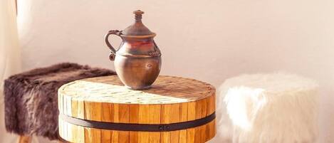A round wooden table with a metal jug on top, flanked by a fur-covered stool and a white fur-covered stool.