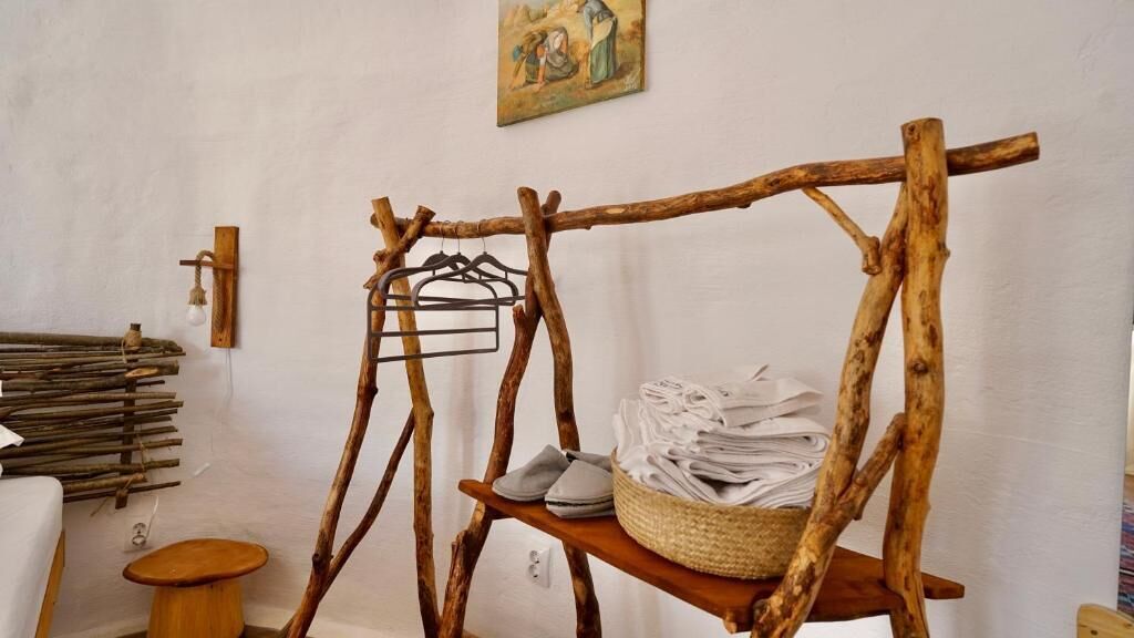 Une étagère en bois rustique avec des serviettes pliées et un panier, un porte-vêtements en bois fixé au mur et un petit tabouret.