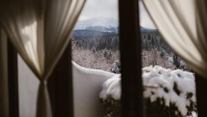 A view through curtains of a snowy landscape with mountains and trees. - Pensiunea Dealul Verde (Sibiu)