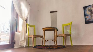 A room with a wooden table and two chairs, a window with white curtains, and a painting on the wall. - Pensiunea Dealul Verde (Sibiu)