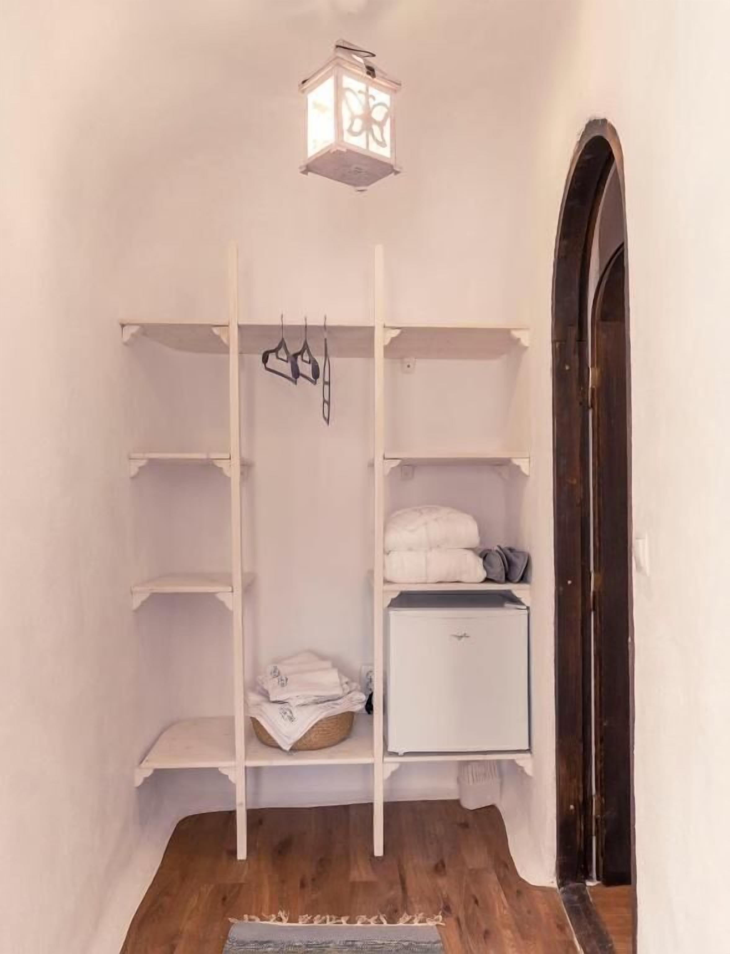 A walk-in closet with open shelving, a hanging rod, and a small white cabinet.