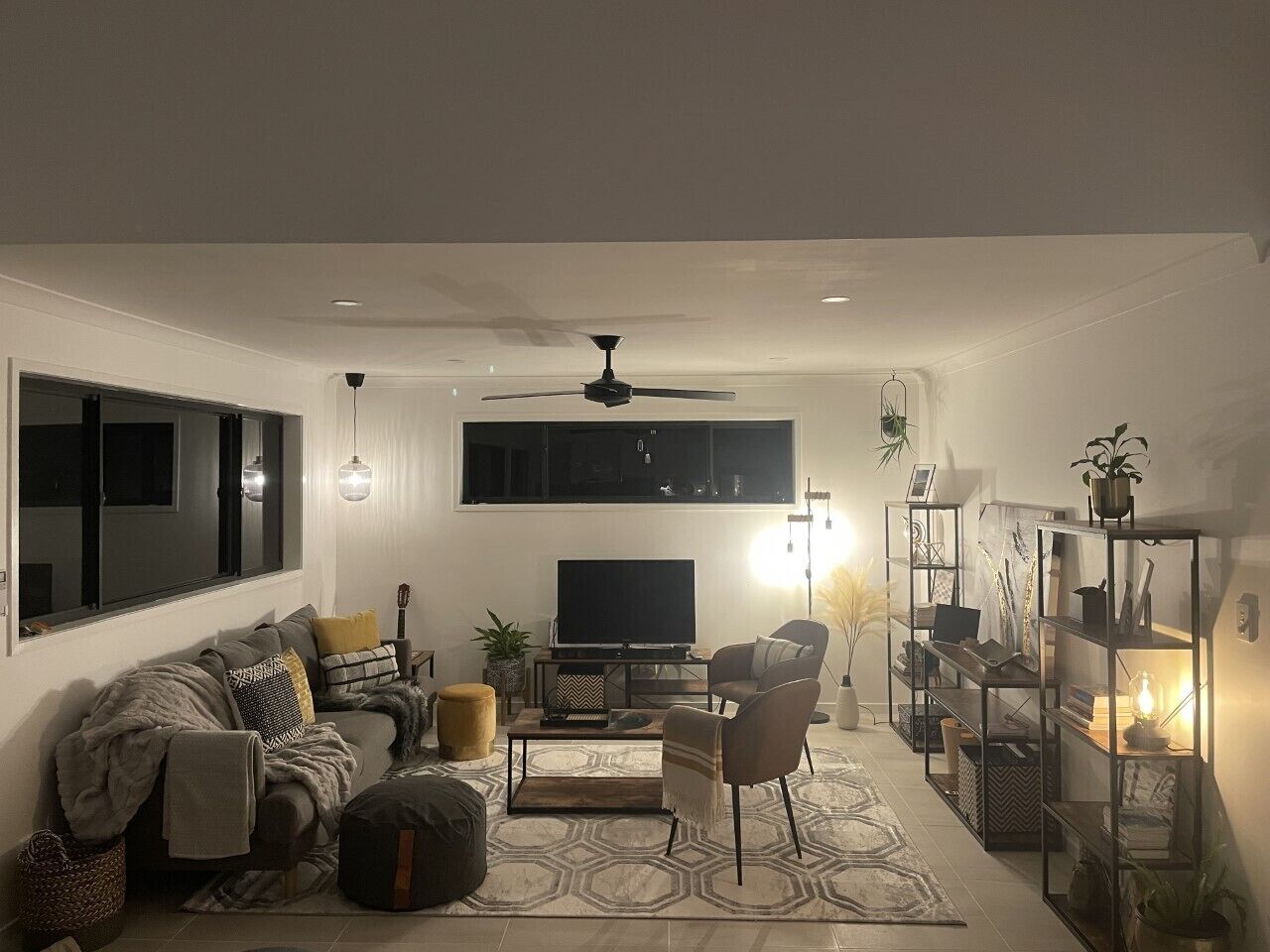 Una sala de estar moderna con sofá, sillón, mesa de centro, televisor y estantería.