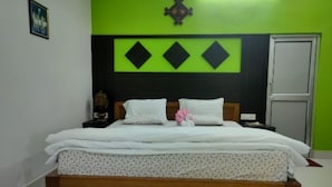 A bed with a floral bedspread, a wooden headboard, and a decorative wall panel above it. - Homocation Changghar Resort (Kaliabar)