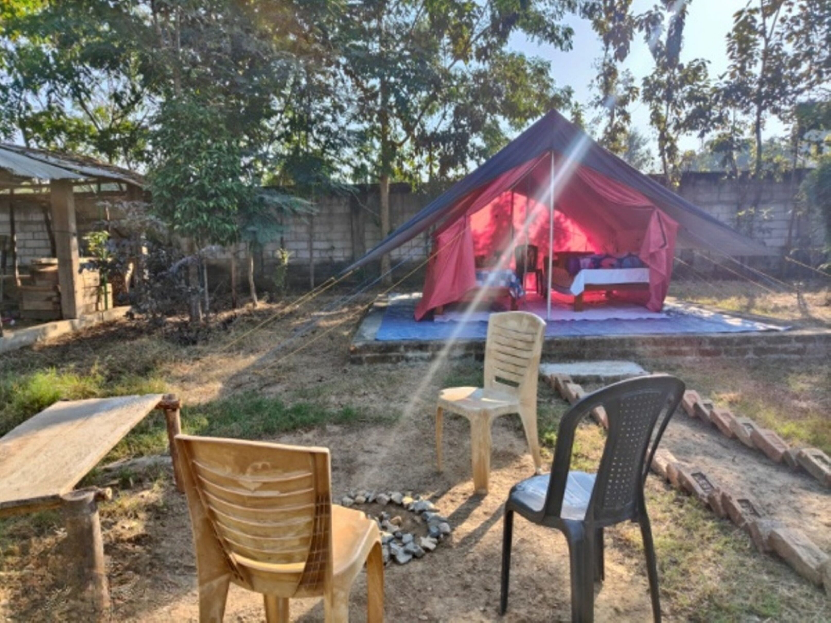 Una tenda con tetto rosso allestita in un giardino, con due sedie e un tavolo.