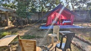 Una tenda con tetto rosso allestita in un giardino, con due sedie e un tavolo.