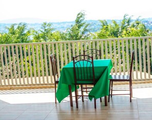 A balcony with a table and chairs covered in green tablecloths, overlooking a scenic view.