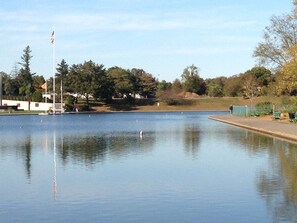 A calm lake with a flagpole, trees, and a distant building.