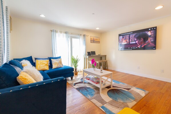 A living room with a blue sofa, a coffee table, and a TV mounted on the wall.