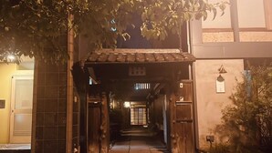 A traditional Japanese building entrance with a wooden gate, tiled flooring, and a covered walkway leading to the main entrance. - This is a single building rental of a Kyomachiya that has been in existence since the Meiji Era (1868-1912). The window overlooks the Kamo River and the town of Gion, making it a prime location to enjoy the typical Kyoto scenery. (Kyoto)