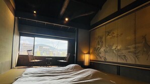 A hotel room with a large bed, a view of the city through a window, and a traditional artwork on the wall. - This is a single building rental of a Kyomachiya that has been in existence since the Meiji Era (1868-1912). The window overlooks the Kamo River and the town of Gion, making it a prime location to enjoy the typical Kyoto scenery. (Kyoto)