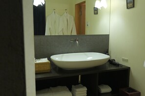 Ein Badezimmer mit einem großen weißen Waschbecken, einem Spiegel, einem Handtuchhalter mit weißen Handtüchern und einem kleinen Holzkorb.