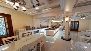 Un amplio hall de hotel con una isla central, mobiliario blanco e iluminación decorativa.