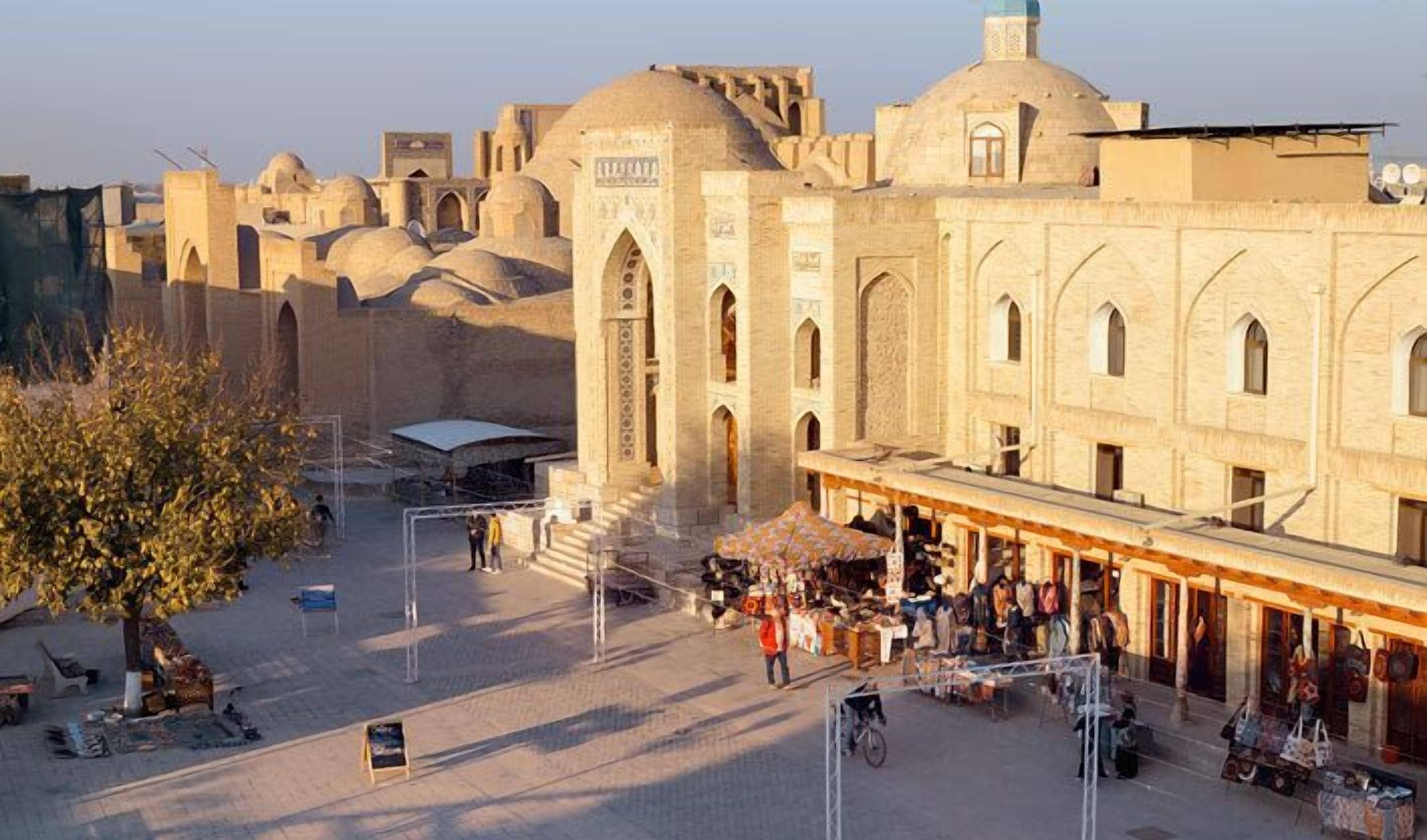 A historic building with arched windows and domed roofs, surrounded by a market area with vendors and stalls.
