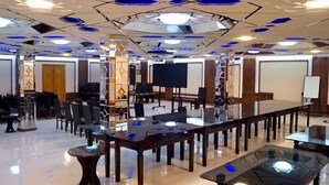 Un salón de conferencias con una mesa de vidrio, sillas, una pantalla de proyector y una pizarra.