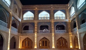 A historical building with multiple arched windows and balconies, featuring intricate stonework and a central open space. - Shahriston (Bukhara)