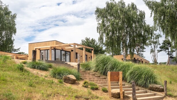 A modern building with a wooden exterior, large windows, and a staircase leading to the entrance. - Luxury Lodge with Beach View (Well)