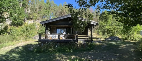 Una cabana de fusta amb un porxo, envoltada d'arbres i sota un cel serè.