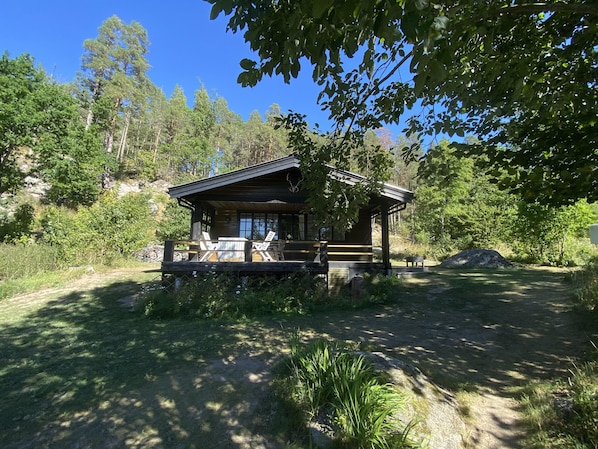 Eine Holzhütte mit Veranda, umgeben von Bäumen und blauem Himmel.
