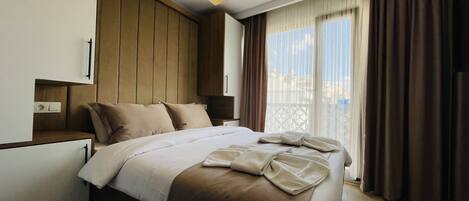 Habitación de hotel con una cama, mesita de noche, televisión y ventana con cortinas.