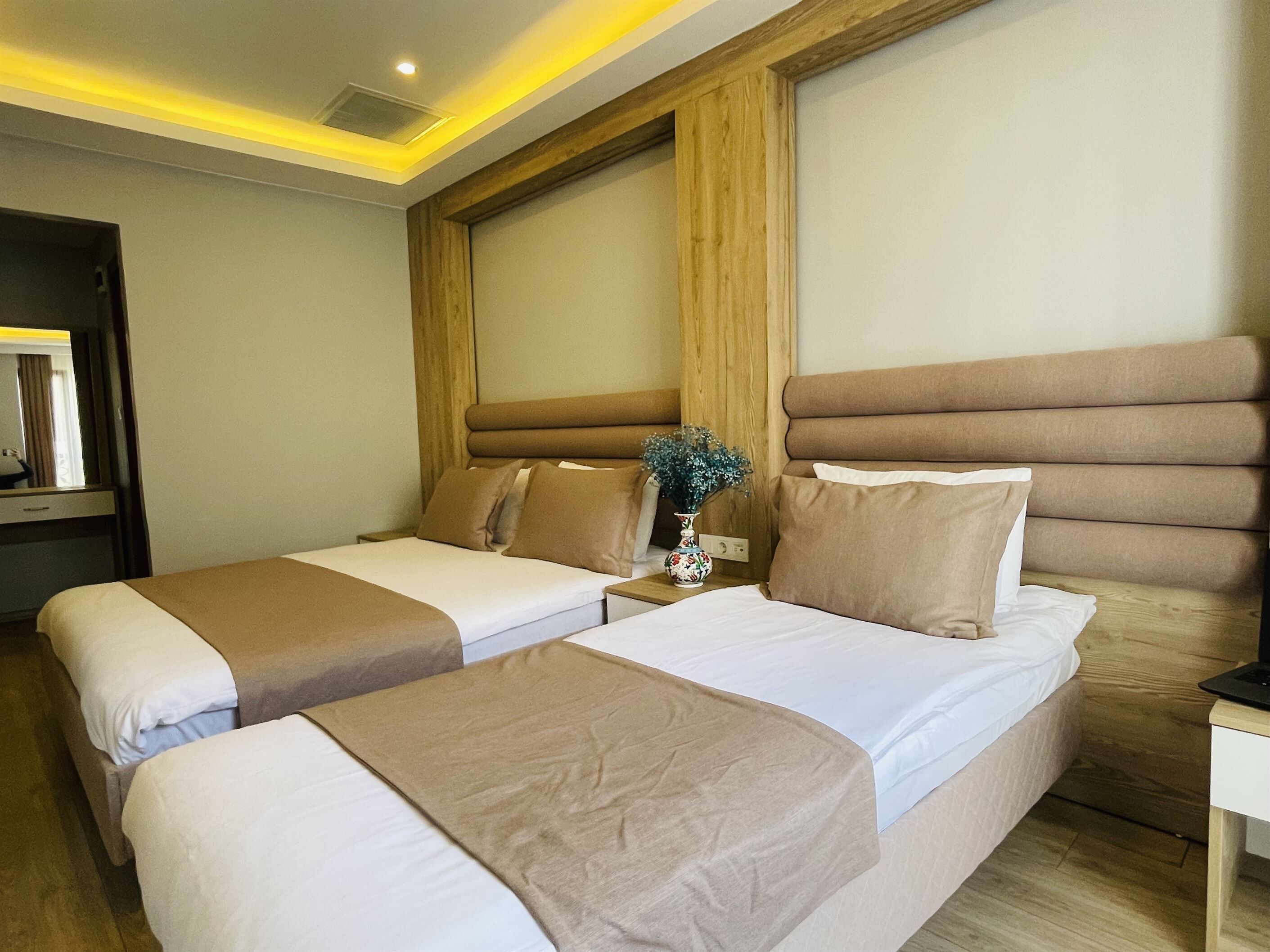 Een hotelkamer met twee bedden, een houten hoofdbord, een nachtkastje met een vaas en een spiegel.