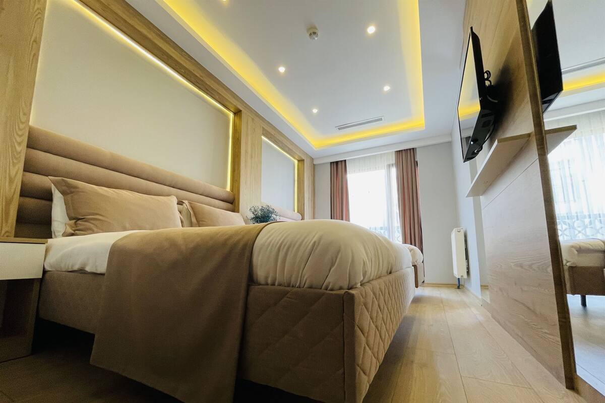 A modern bedroom with a large bed, wooden headboard, and a flat-screen TV mounted on the wall.