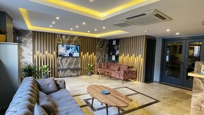 A modern lobby with a grey sofa, a wooden coffee table, and a TV mounted on a wall with vertical light strips. - Zem Hotel (Istanbul)