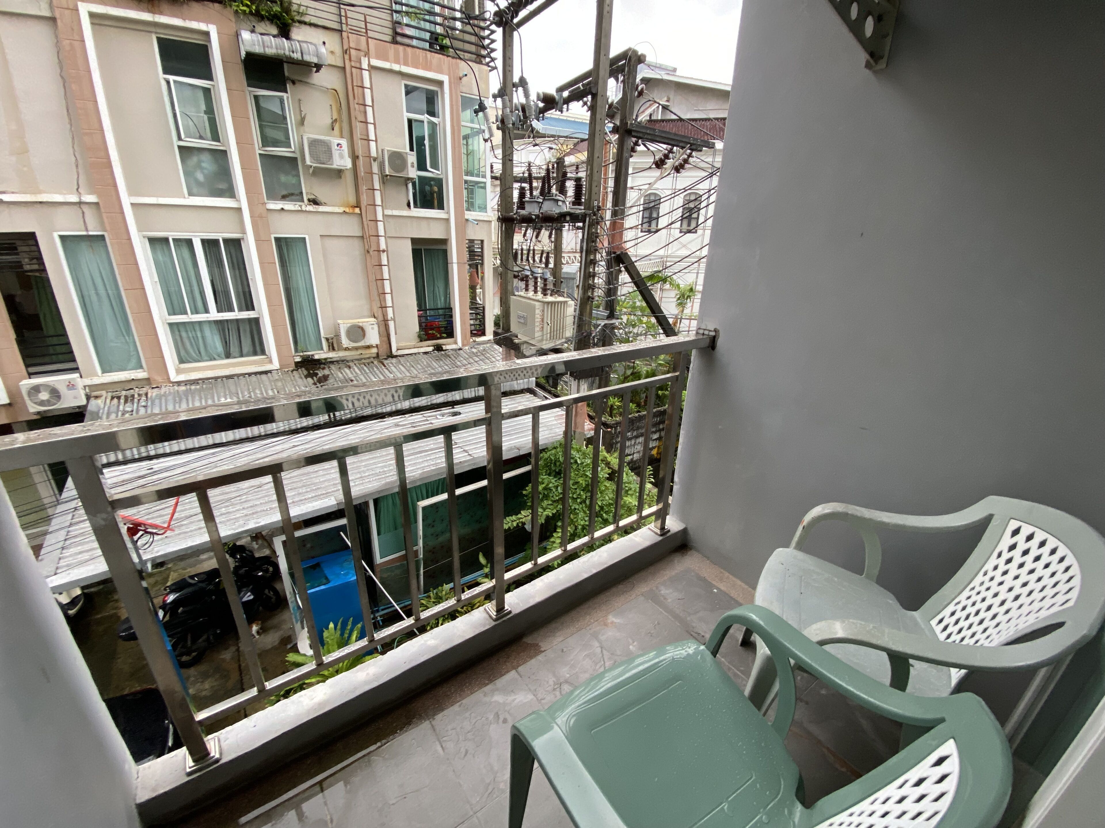 En balkon med gelænder, en grøn plastikstol og en hvid plastikstol.