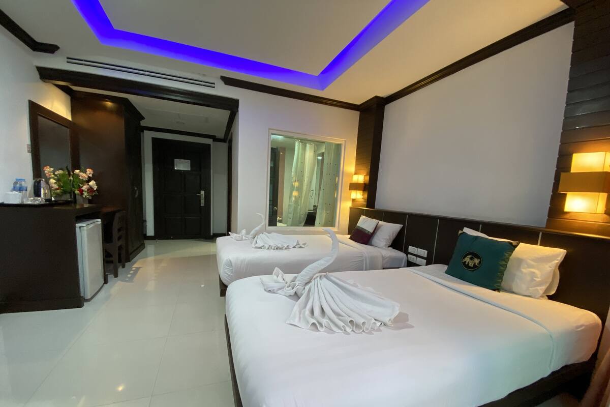 Ein Hotelzimmer mit zwei Betten, einem Schreibtisch mit Stuhl und einer kleinen Küchenzeile.