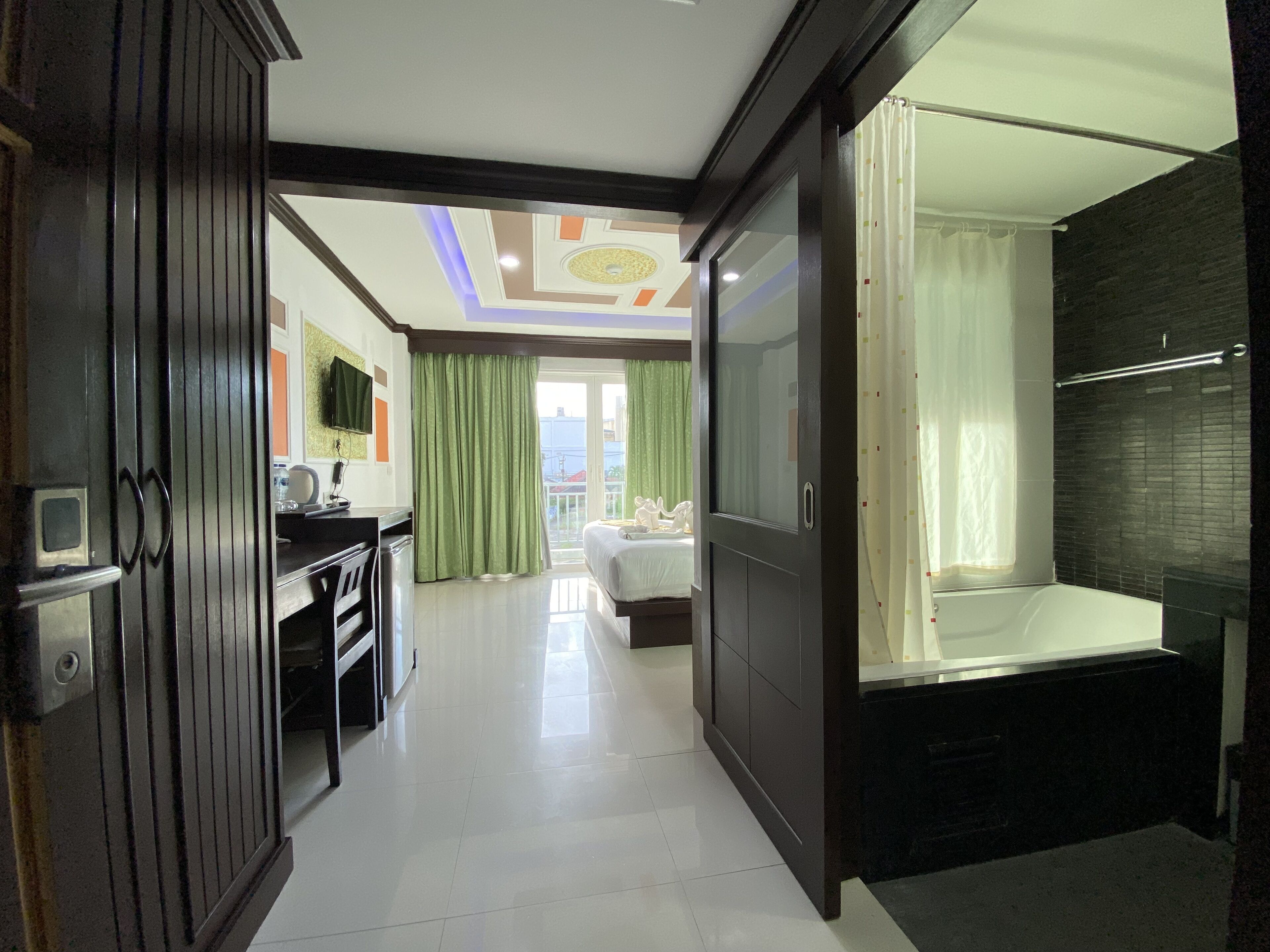 A hotel room with a large bed, a desk with a chair, a wardrobe, and a bathroom with a bathtub.