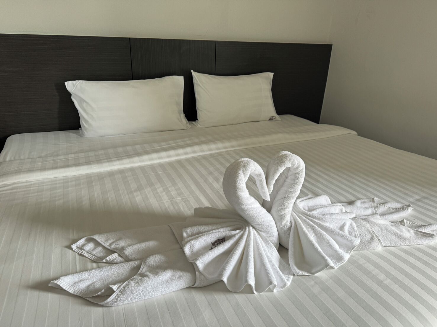 Una cama bien hecha con ropa de cama a rayas y dos almohadas, un cabecero oscuro y una toalla doblada sobre la cama.