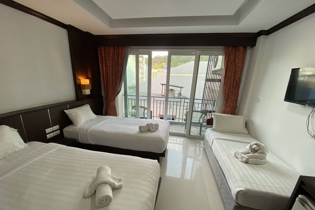 Ein Hotelzimmer mit zwei Betten, einem Fernseher und einem Balkon mit Tisch und Stühlen.