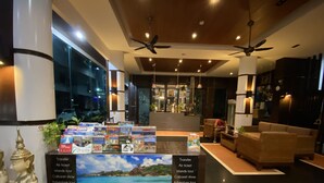 A lobby with a reception desk displaying travel brochures, a seating area with a sofa and chairs, and ceiling fans. - 77 Patong Hotel & Spa (Patong)