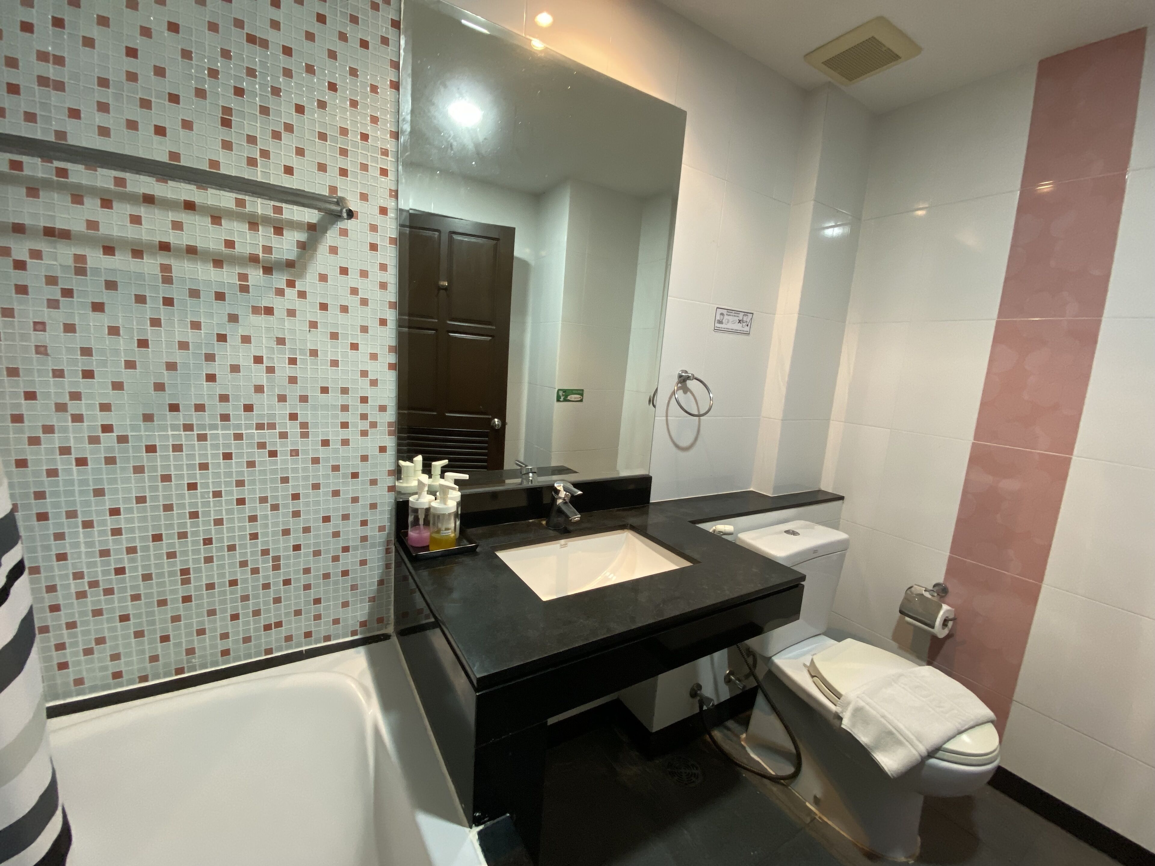 A modern bathroom with two sinks, a bathtub, a toilet, and a large mirror.