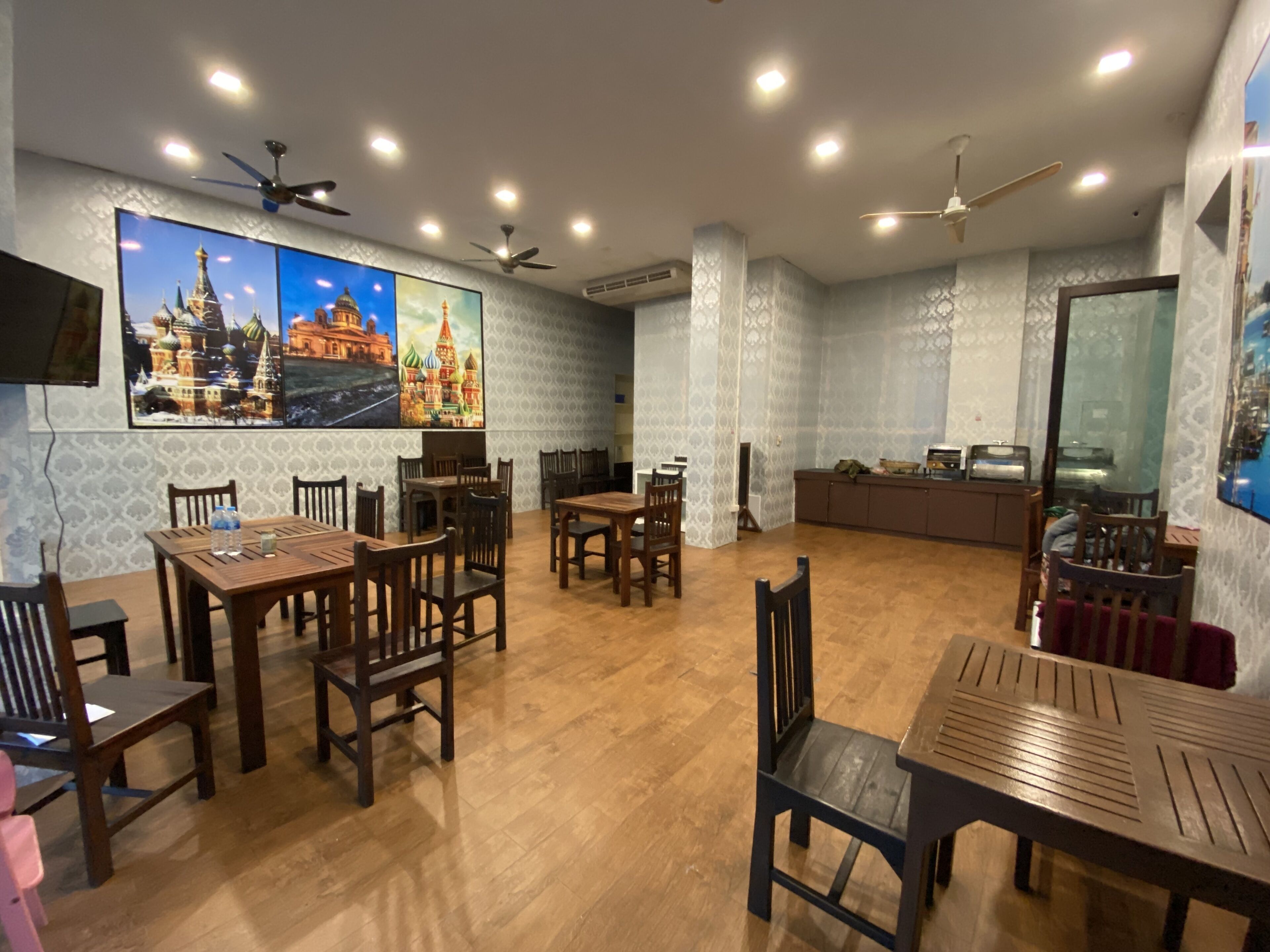 A spacious dining area with wooden tables and chairs, a large wall-mounted TV, and ceiling fans.