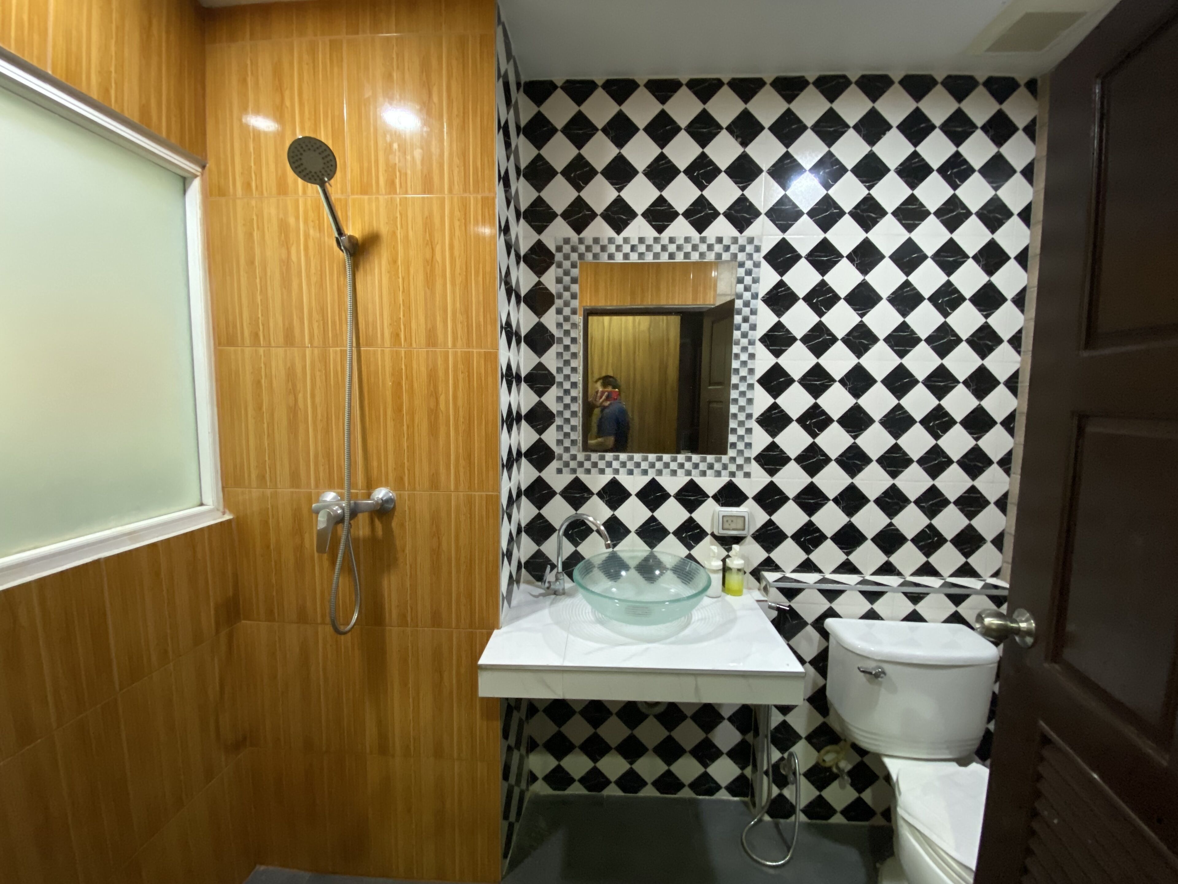 A bathroom with a wooden shower enclosure, a sink with a glass basin, and a toilet.