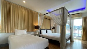 A double bed with a canopy, a bedside table with a lamp, and a view of the outside through a large window. - 77 Patong Hotel & Spa (Patong)